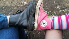 two people wearing black and pink shoes with green laces on their feet, one is holding the other's leg