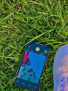 a cell phone laying on the grass next to someone's shoes and tennis shoe