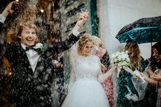 a bride and groom walking through the rain with their arms in the air as they are surrounded by confetti