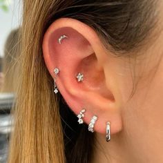 a woman's ear is adorned with small silver leaves and cubicnes on it