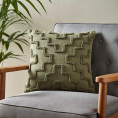 a green pillow sitting on top of a gray chair next to a potted plant