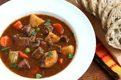 a bowl of beef stew with bread on the side