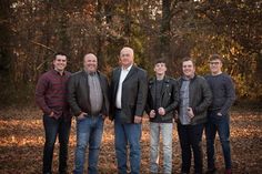 a group of men standing next to each other in front of trees and fallen leaves