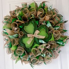 a wreath made out of burlocks and green ribbon hanging on a white door