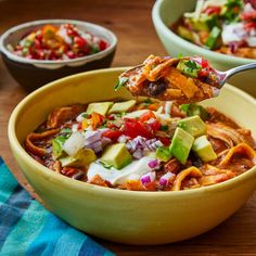 a spoon full of mexican soup with tortilla chips and avocado on the side