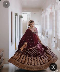 a woman in a maroon and gold lehenga is walking down the hall with her hand on her hip