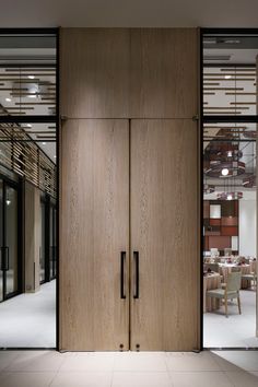 two wooden doors are open in front of a dining room with glass walls and tables