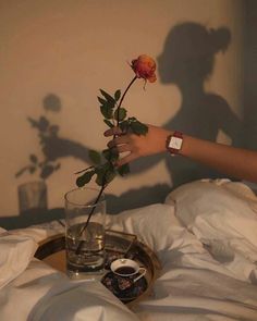 a person reaching for a rose in a glass vase on a bed with white sheets