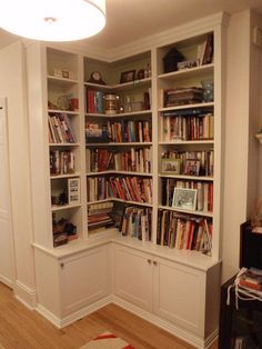 a living room filled with lots of books on top of white bookcases next to a doorway