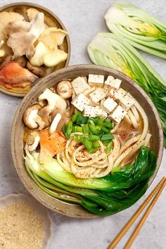 two bowls filled with noodles and vegetables next to chopsticks on a white surface