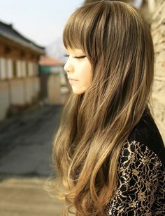 a woman with long hair standing next to a wall and looking off into the distance