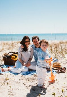 a man and woman are sitting on the beach with a child in front of them