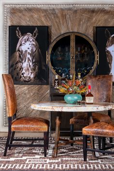 a dining room table with chairs and pictures on the wall behind it, along with two horse heads