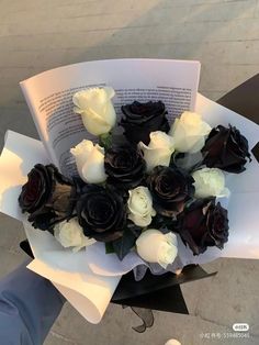 a bouquet of white and black roses on top of an open book in someone's hand