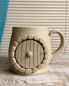 a ceramic cup with a hole in the middle on top of a wooden table next to blinds