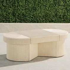 a round table sitting on top of a cement floor next to a green hedge covered wall