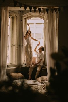 a man and woman sitting on a window sill with their arms in the air