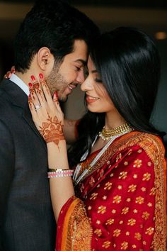 a man and woman standing next to each other in front of a bed with their arms around each other