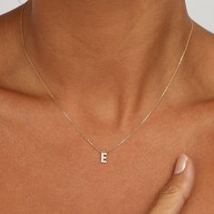 a woman wearing a necklace with the letter e on it's chest and holding her hand up to her chest