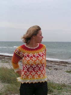 a woman standing on top of a sandy beach next to the ocean with her hands in her pockets