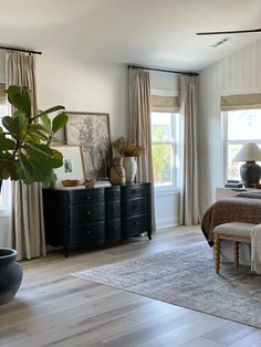 a bed room with a neatly made bed next to two windows and a potted plant