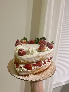 a person holding a cake with strawberries on top