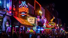 people are walking down the street at night in an area that has many neon signs