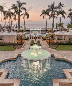 a large fountain in the middle of a lawn with chairs and palm trees around it