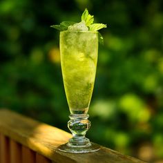 a tall glass filled with green liquid sitting on top of a wooden fence