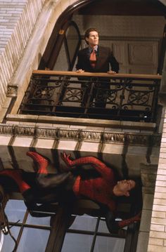 a man standing on top of a balcony next to a spiderman statue in front of him