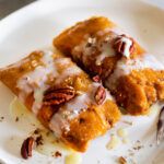 two pieces of dessert sitting on top of a white plate with pecans and icing