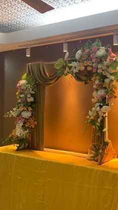 a yellow table topped with flowers and greenery next to a gold cloth covered wall