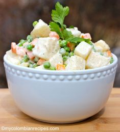 a white bowl filled with peas, carrots and tofu salad on top of a wooden table