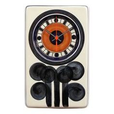 an orange and black clock on a white wall with four speakers in front of it