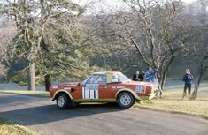 an old race car is parked on the side of the road in front of some people