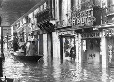 an old black and white photo of people in a boat floating down a flooded street