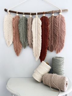 several yarns are hanging on a wall next to a white table with a wooden stick