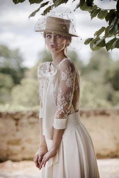 a woman in a white dress and hat standing under a tree with her hands on her hips