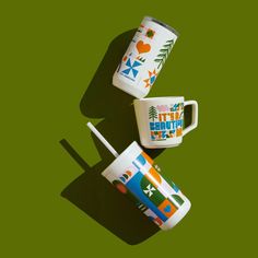 two coffee mugs sitting next to each other on a green surface