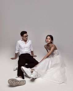 a man and woman sitting on the ground next to each other in white dresses with shoes