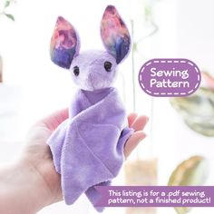 a hand holding a purple stuffed animal with ears