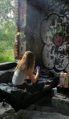 a woman sitting in an outdoor hot tub with graffiti on the wall behind her and looking at her cell phone