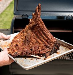 a person is holding a tray with food on it and an open grill door in the background