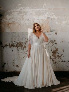 a woman in a white dress is posing for a photo with an old wall behind her