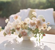 a white vase filled with lots of flowers on top of a wooden table next to a couch