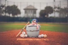 a baby sitting in a bucket with baseballs and a bat on the ground next to it