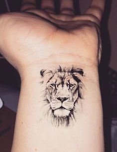 a lion tattoo on the wrist is shown in black and grey ink, with an animal's face drawn across it