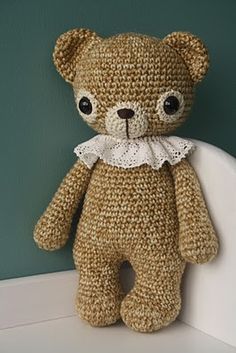 a crocheted teddy bear sitting on top of a white shelf next to a green wall