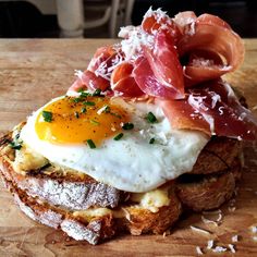 an open face sandwich topped with bacon, eggs and cheese on a wooden cutting board