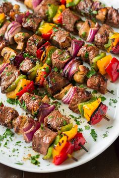 skewered meat and vegetables on a white plate with parsley sprinkled around them